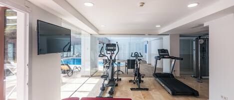 A modern home gym with exercise equipment, a TV, and a large window overlooking a pool.