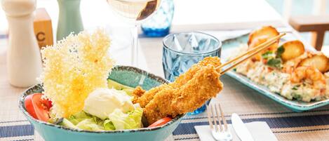 Una mesa de comedor con un tazón azul que contiene una ensalada, un alimento frito y una copa de vino blanco.