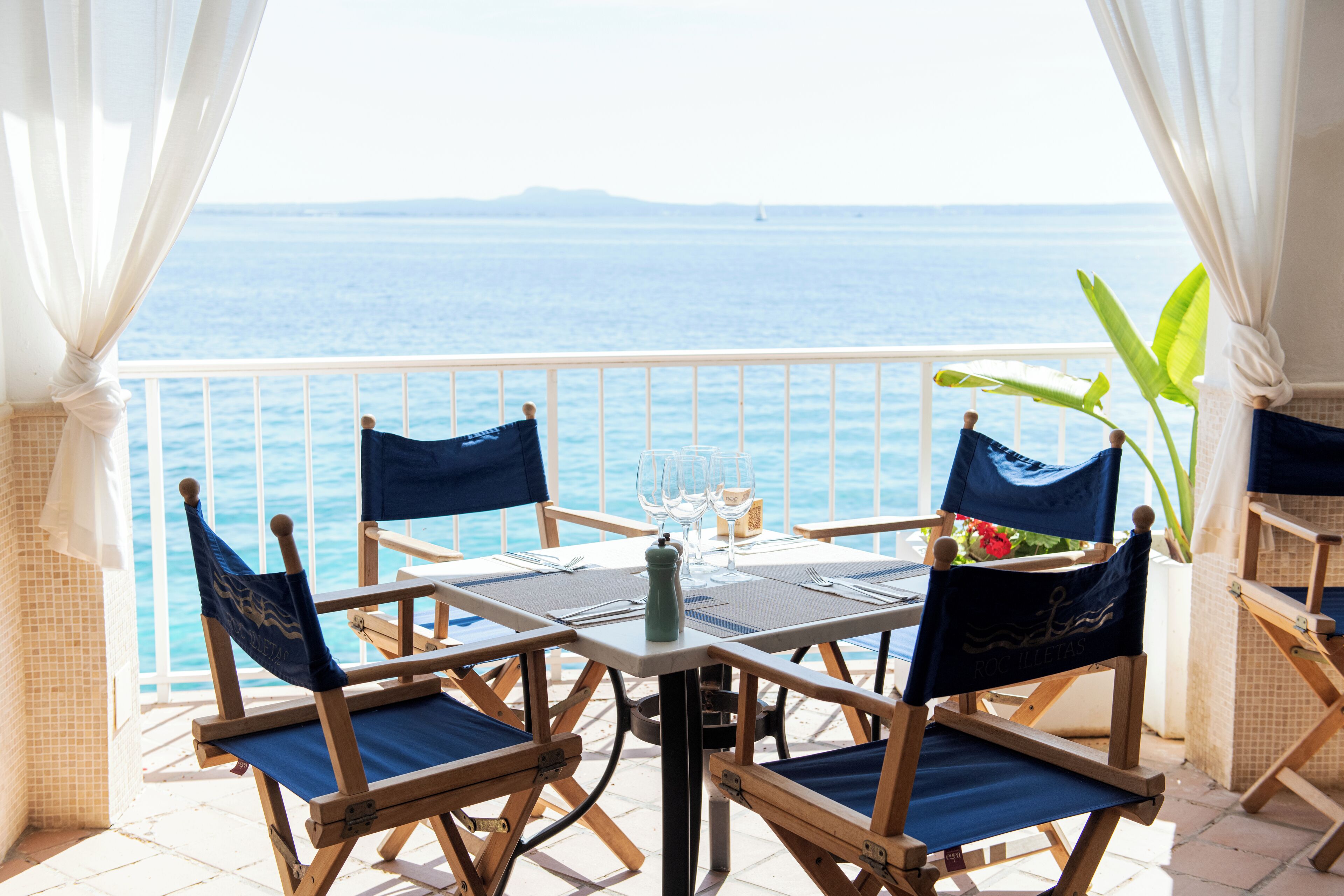 A balcony with a table set for two, overlooking the sea.