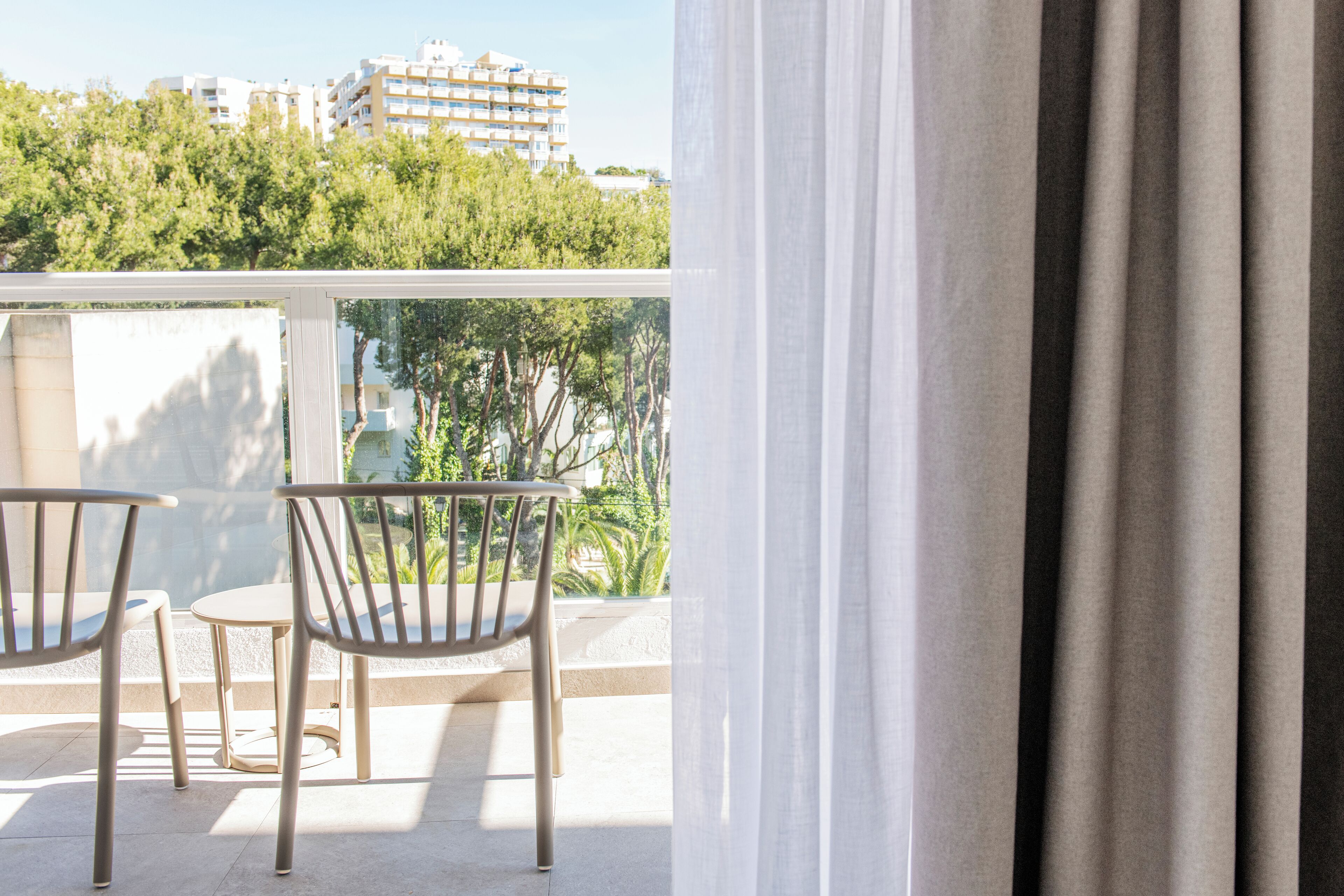 A balcony with two chairs and a table, overlooking a building and trees.