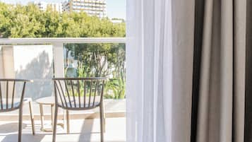A balcony with two chairs and a table, overlooking a building and trees.