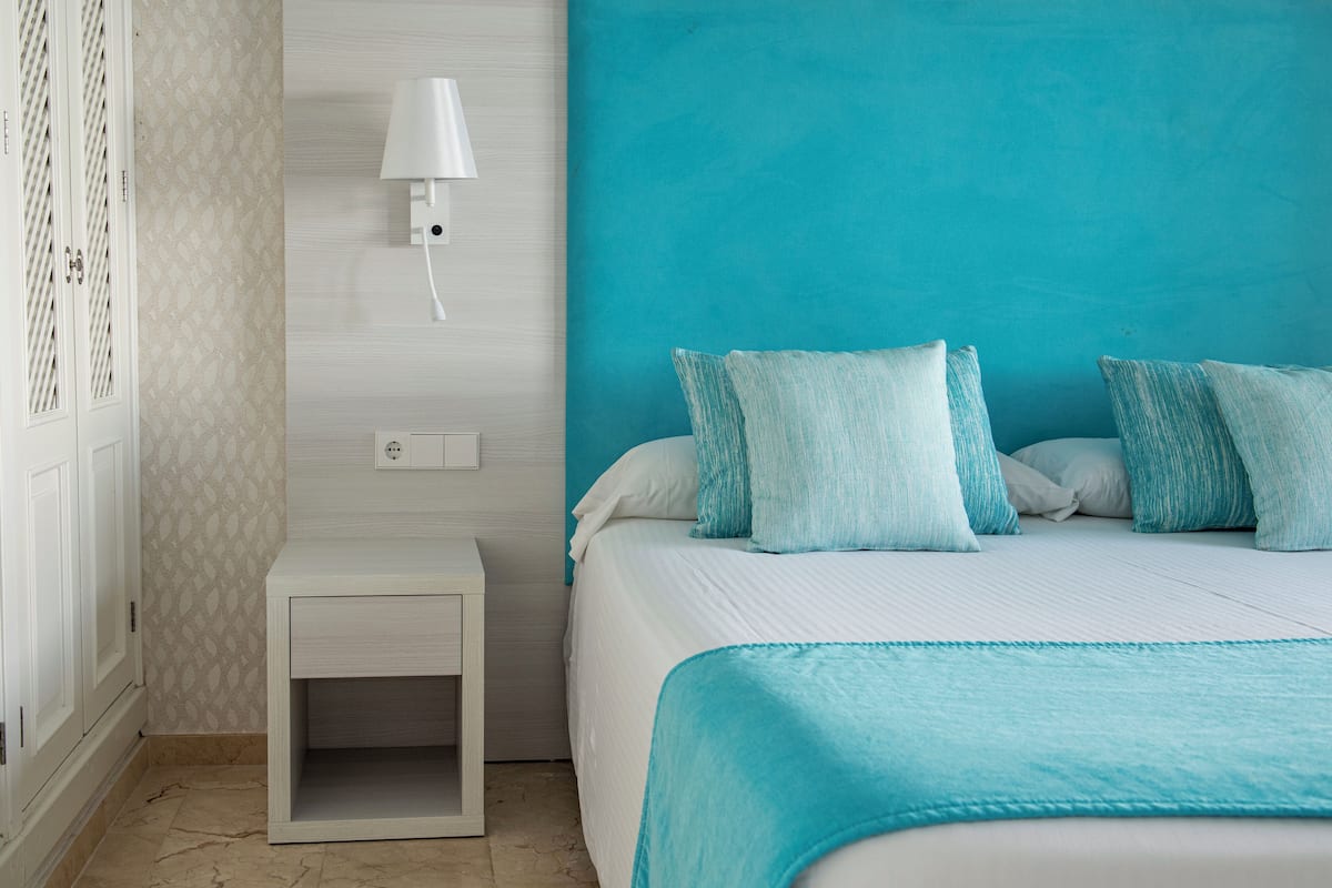 A bedroom with a bed, a nightstand, a wall-mounted lamp, and a teal-colored wall.