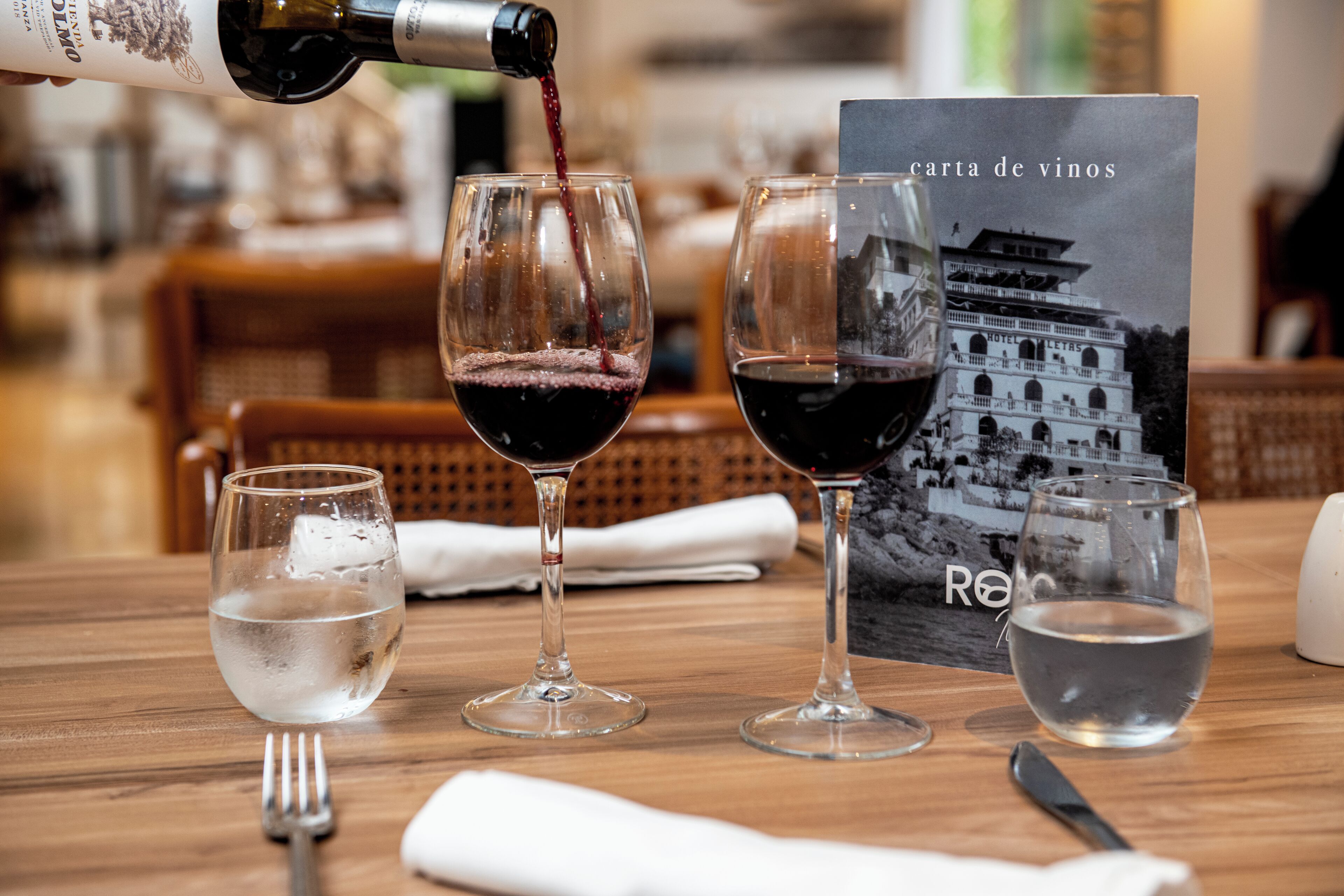 Una mesa con copas de vino, una botella y un menú.