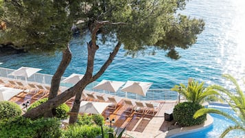 A poolside area with lounge chairs and umbrellas, surrounded by trees and overlooking a body of water.