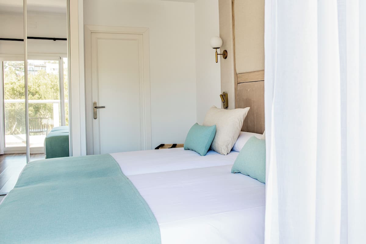 A bedroom with a bed, pillows, a nightstand, a lamp, and a door.