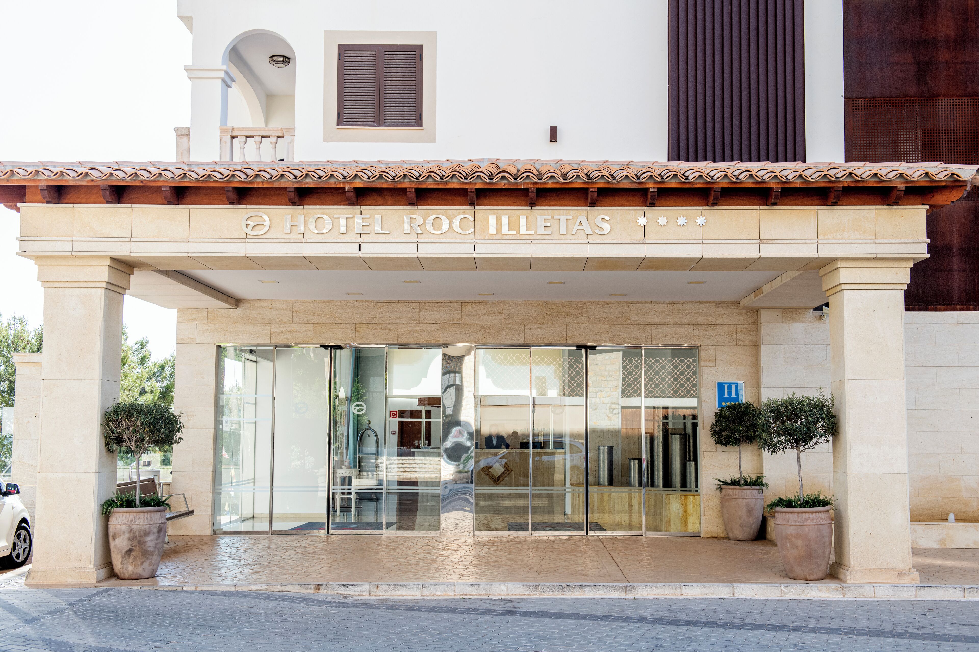 L’entrée de l’hôtel Roc Illetas, avec son toit recouvert de tuiles, ses portes vitrées et ses plantes en pot.
