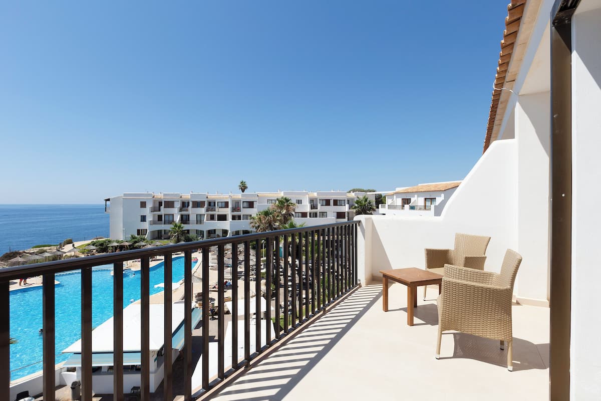 A balcony with a pool, outdoor furniture, and a view of the ocean and hotel buildings.