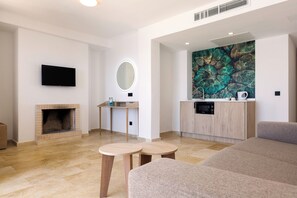 A modern living room with a fireplace, a flat-screen TV, a round mirror, a kitchen area with a microwave, and a large abstract painting on the wall. - Alua Suites las Rocas (Santanyi)