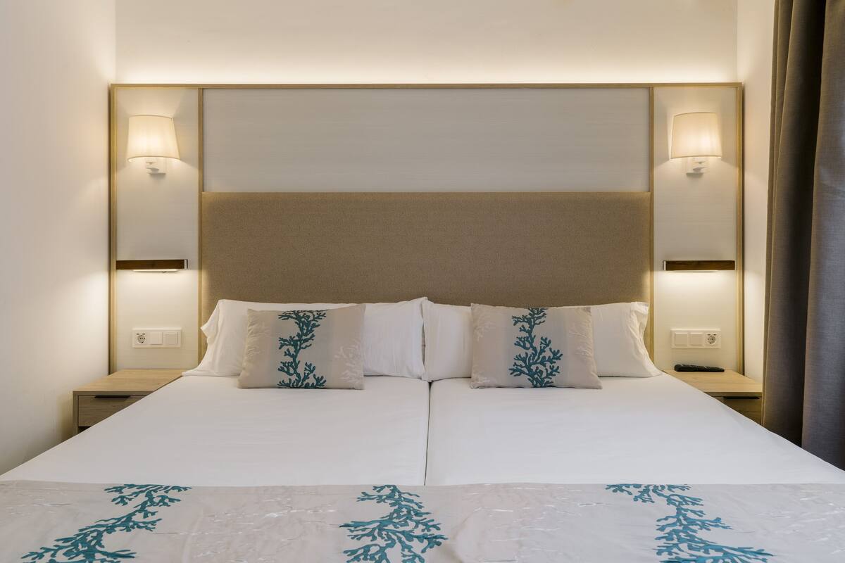 A double bed with a headboard, two bedside lamps, and decorative pillows.