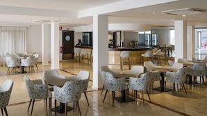 A spacious hotel lobby with a reception area, multiple seating arrangements, and a bar. - Alua Suites las Rocas (Santanyi)
