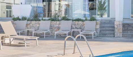 A poolside area with lounge chairs and a stone wall.