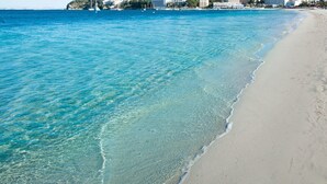 A beach with clear turquoise water, a sandy shore, and buildings in the background. - Suites ROC Portonova - Newly Renovated 2026 (Calvia)