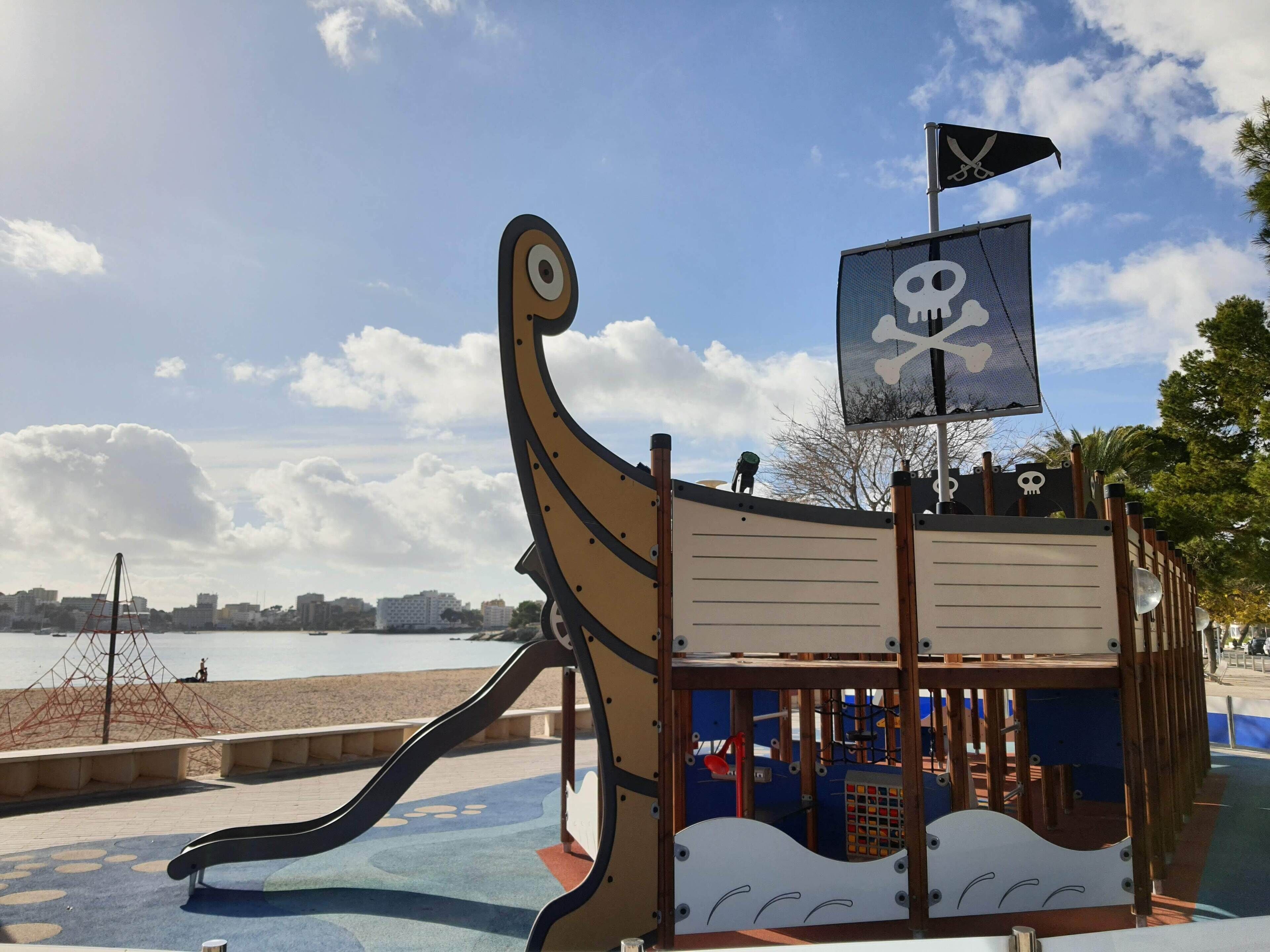 Une structure de jeu sur le thème des pirates, avec un toboggan et un drapeau orné d’un crâne et de deux os croisés.