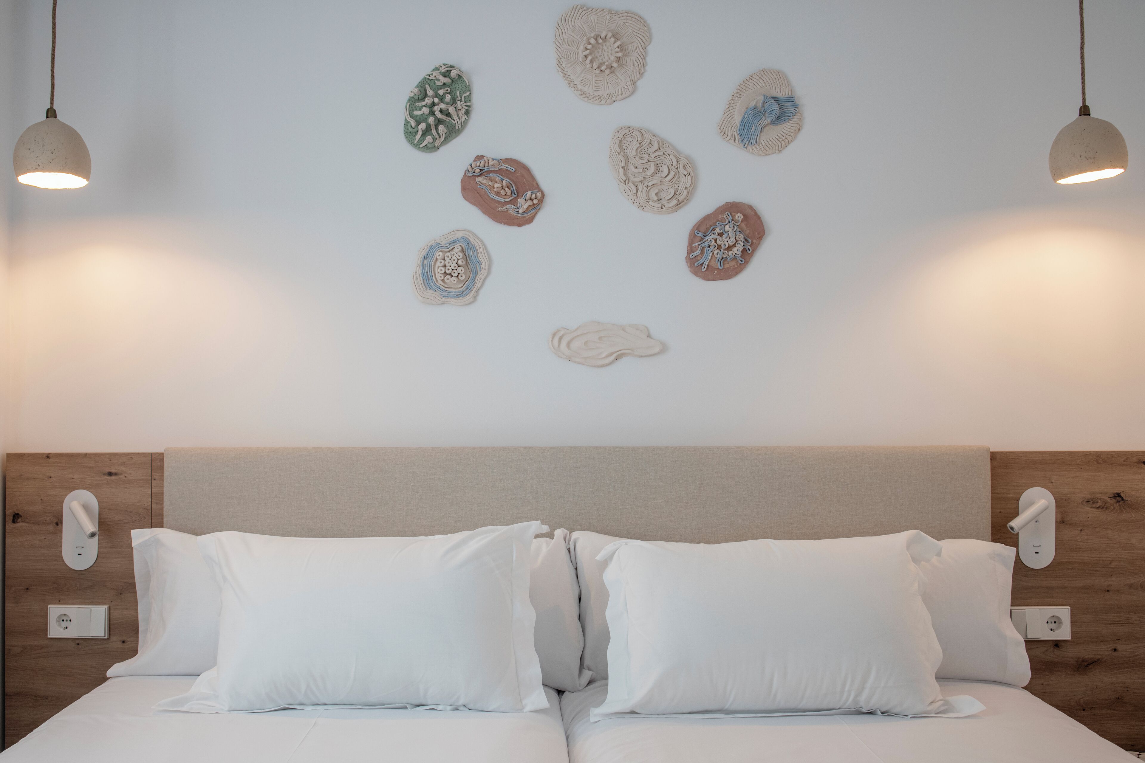 A bedroom with a wooden headboard, two white beds with pillows, and wall-mounted light fixtures.
