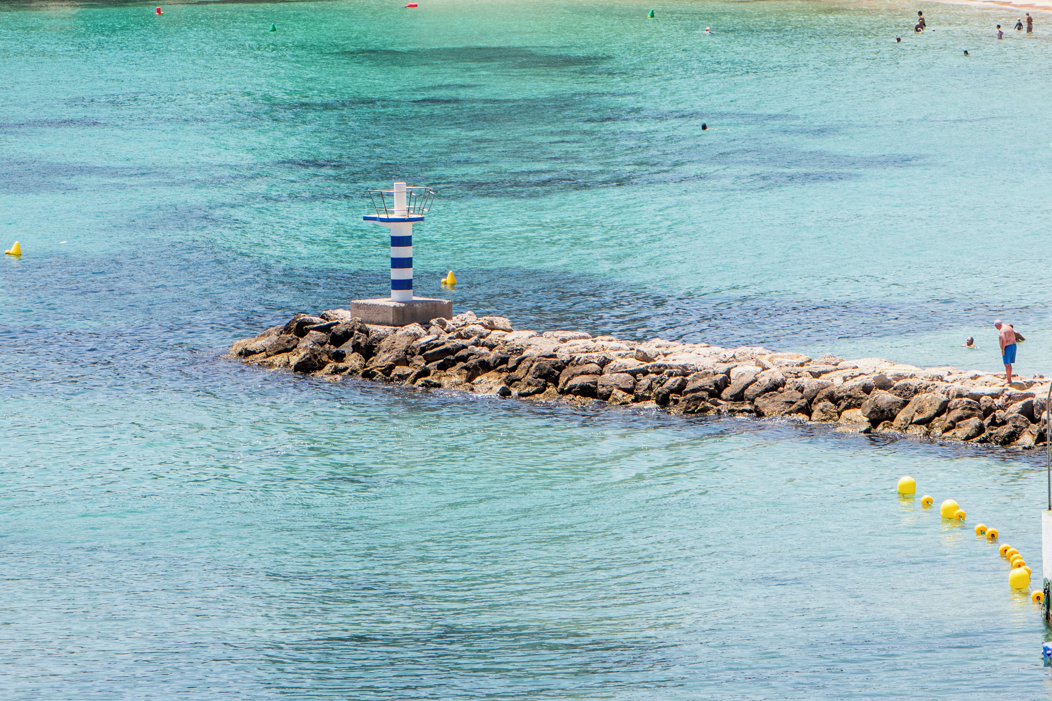 Une jetée s’avançant dans une mer d’un bleu limpide, avec un phare à son extrémité.