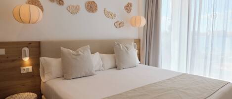 A modern hotel room with a large bed, a wooden headboard, decorative wall art, and a round side table.