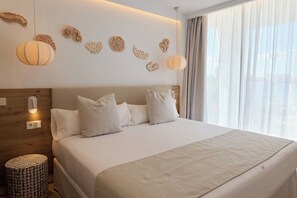 A modern hotel room with a large bed, a wooden headboard, decorative wall art, and a round side table.