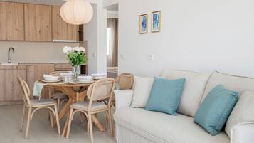 Een moderne keuken met houten kasten, een eettafel gedekt met witte borden en een bloevas, en een lichtgekleurde bank met blauwgroene kussens.