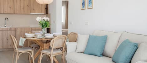 Una cocina moderna con armarios de madera, una mesa de comedor con platos blancos y un jarrón de flores, y un sofá de color claro con almohadones turquesa.