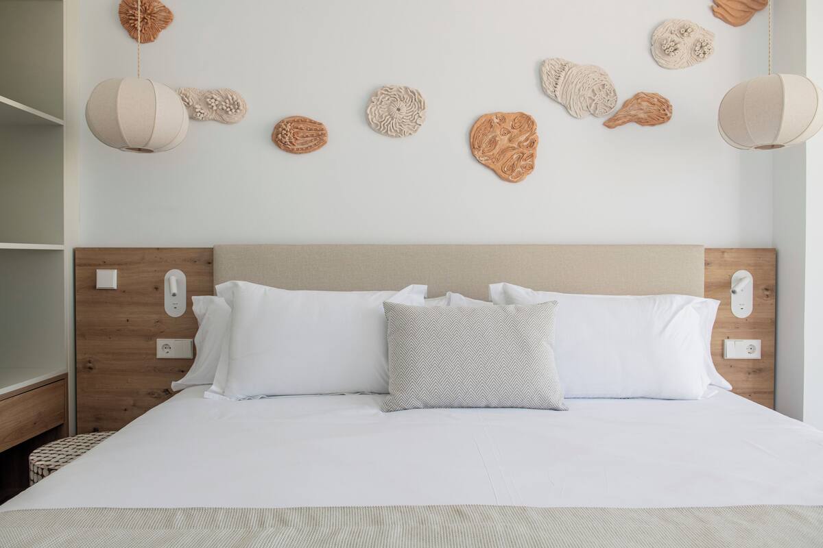 A neatly made bed with white linens and a patterned pillow, a wooden headboard, and wall-mounted decorative items.