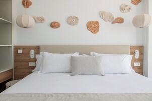 A neatly made bed with white linens and a patterned pillow, a wooden headboard, and wall-mounted decorative items.
