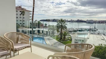 Un balcón con sillones de mimbre y una mesa, con vistas a un puerto deportivo con barcos y un horizonte urbano.