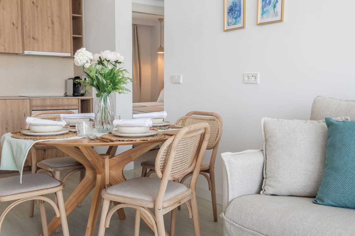 A dining area with a wooden table, wicker chairs, and a vase with flowers.