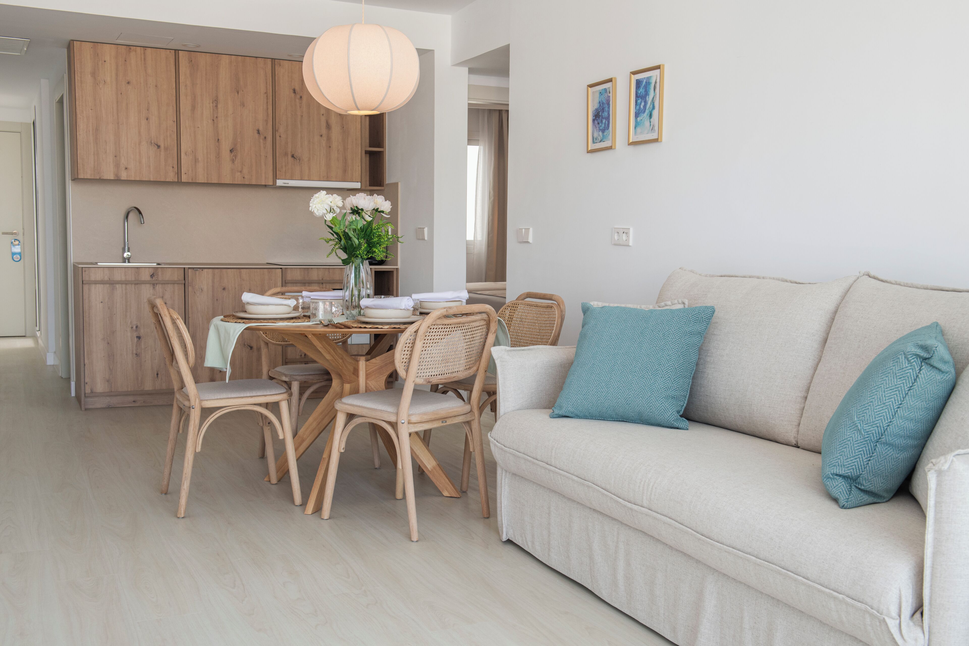 Una cocina moderna con armarios de madera, una mesa de comedor con sillas y un sofá de tonos claros con cojines azules.