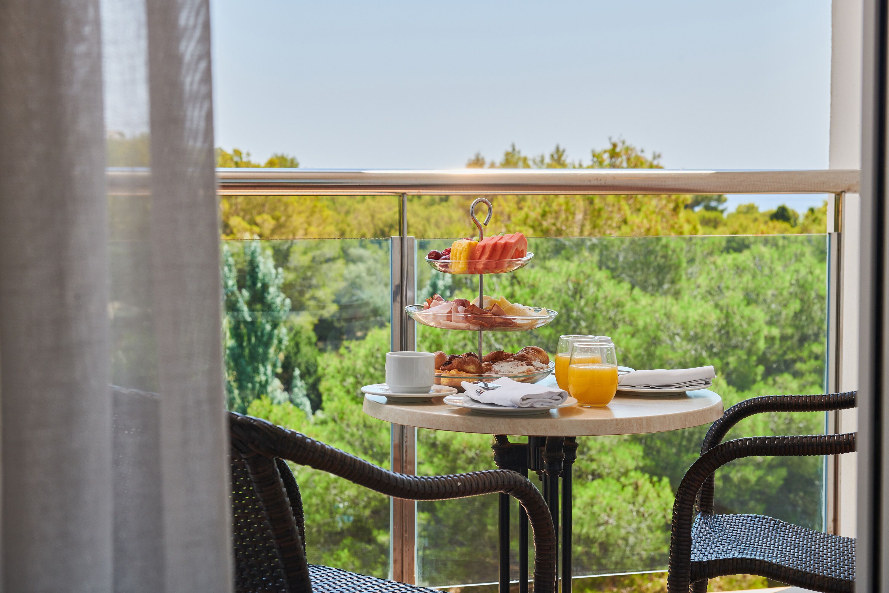 A breakfast table with a three-tiered fruit and cheese board, a cup, a plate with bacon and eggs, and a glass of orange juice.