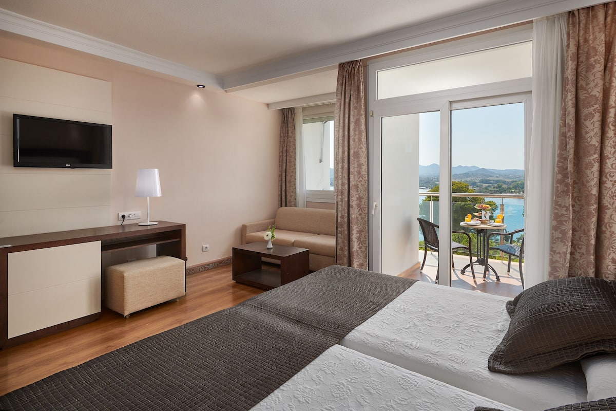Une chambre d’hôtel comprenant un lit, un bureau, une chaise, une télévision et un balcon avec une table et des chaises.