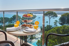Un plateau de petit-déjeuner comprenant une assiette de fruits, des croissants et du jus d’orange, disposé sur un balcon donnant sur une piscine et des arbres.
