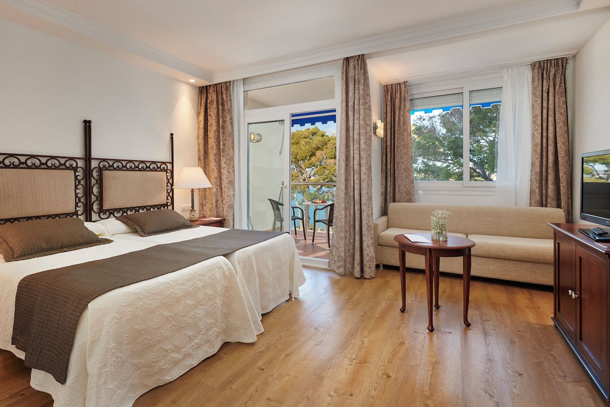 Une chambre d’hôtel avec un grand lit, un canapé, une télévision et un balcon équipé d’une table et de chaises.