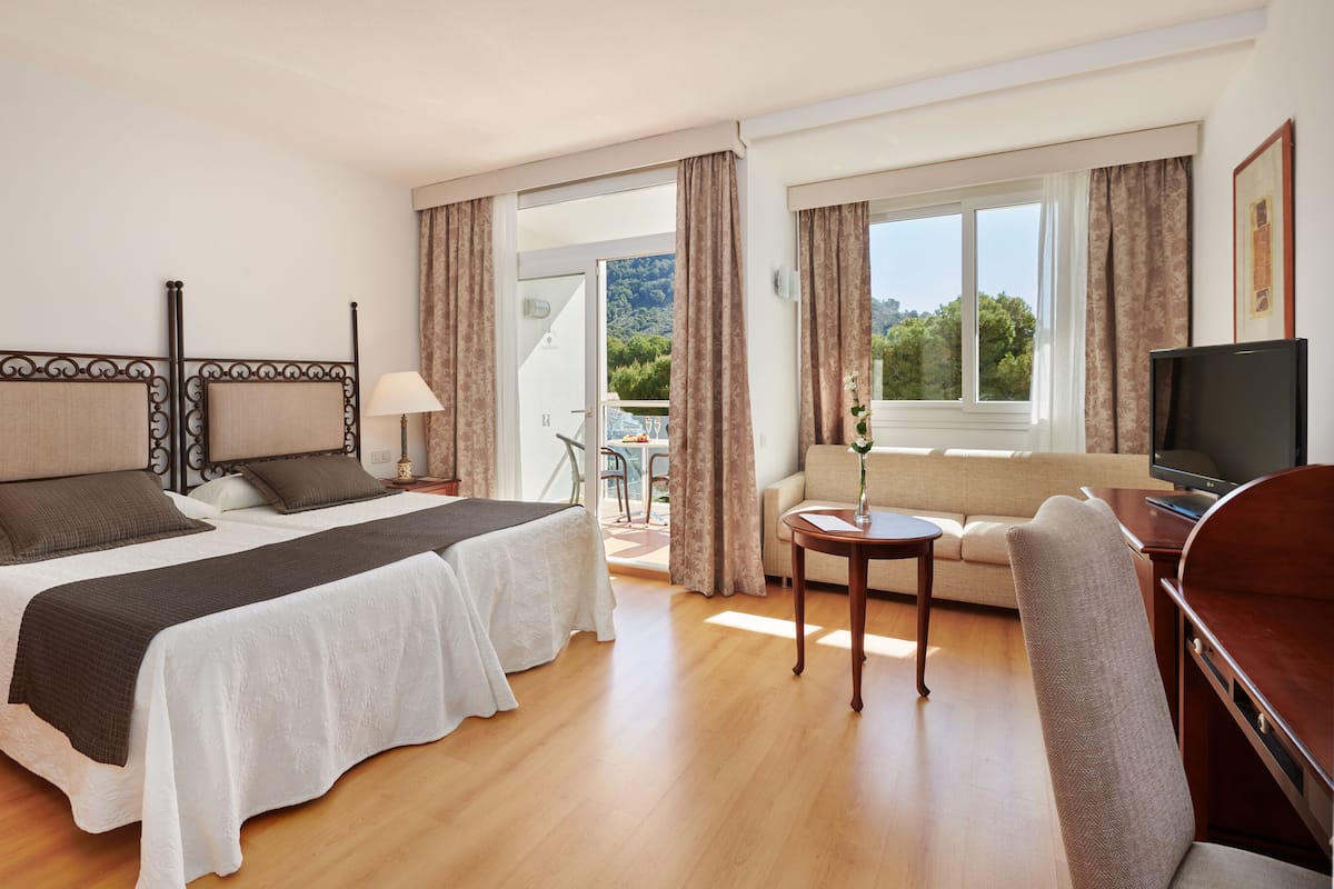 Une chambre d’hôtel équipée d’un lit, d’un bureau, d’une télévision et d’un balcon avec une table et des chaises.