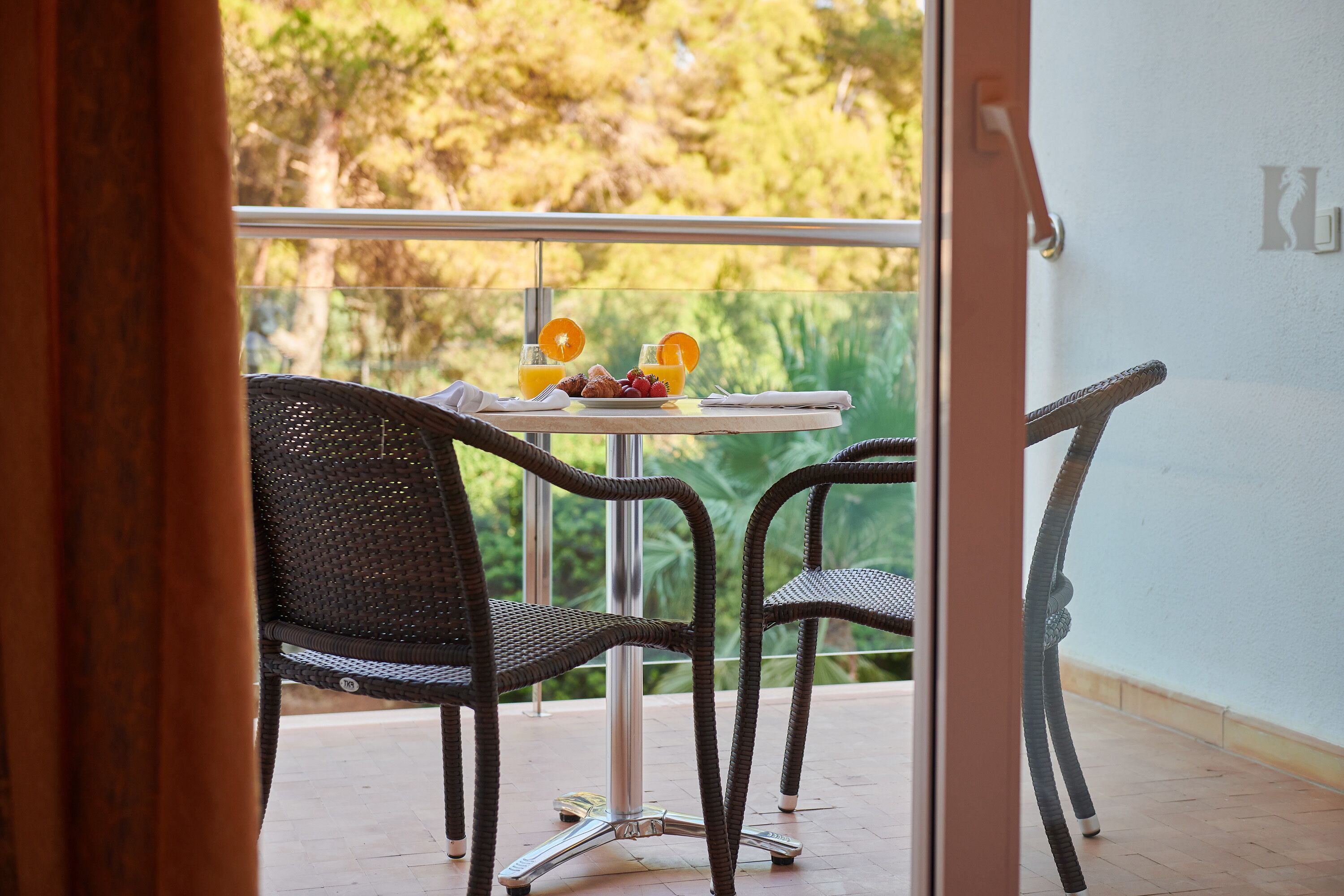 A balcony with wicker chairs and a table set with fruit and orange juice.