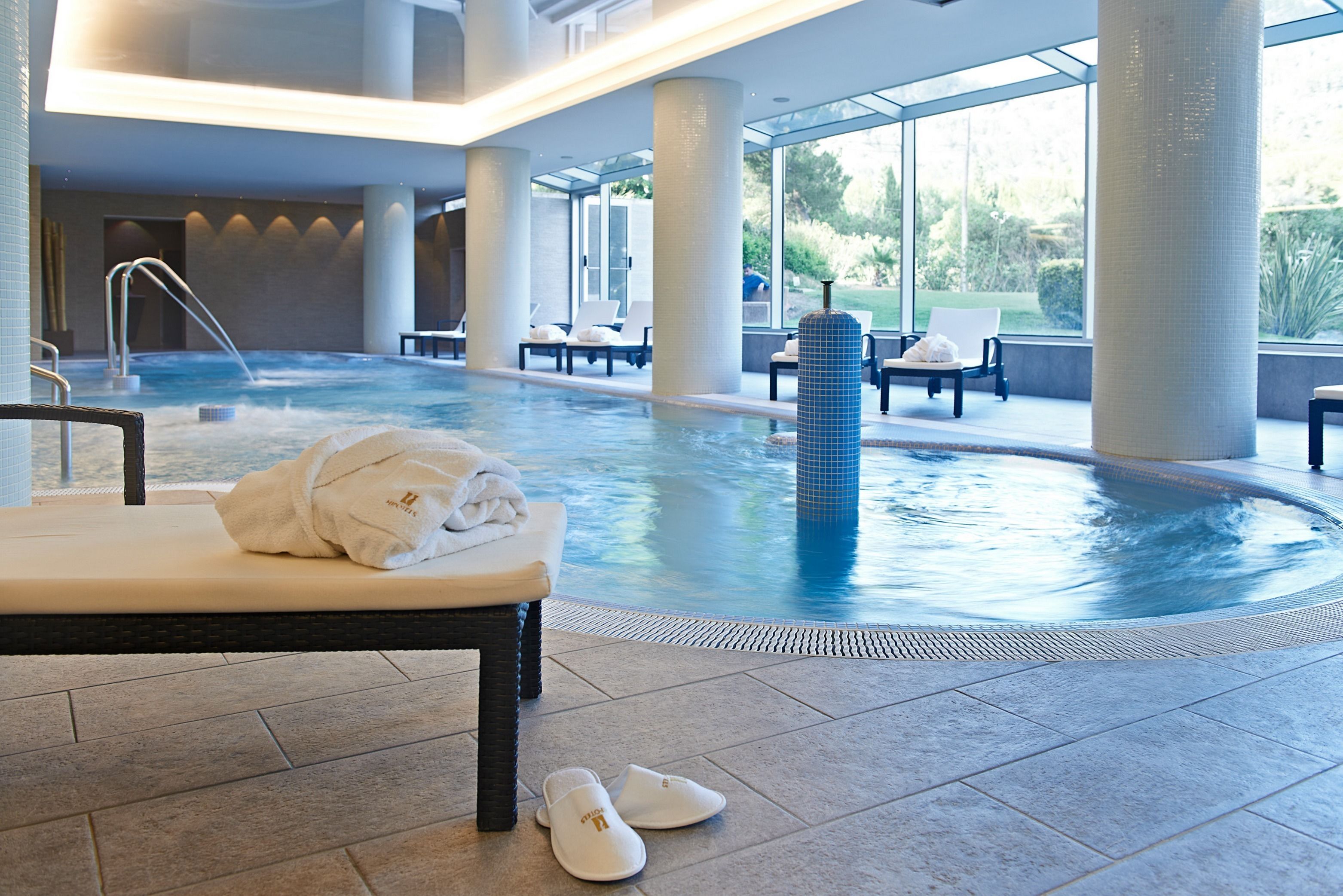 A modern indoor pool area with a lounge chair, a towel, and slippers on the floor.
