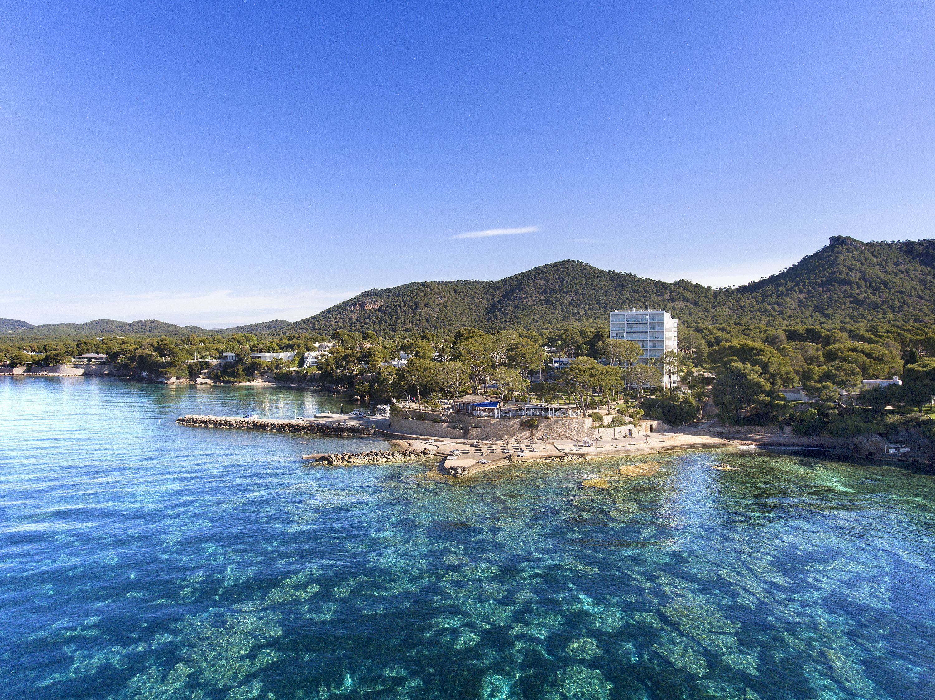 A coastal area with clear blue waters, a rocky shoreline, and a building with multiple floors.