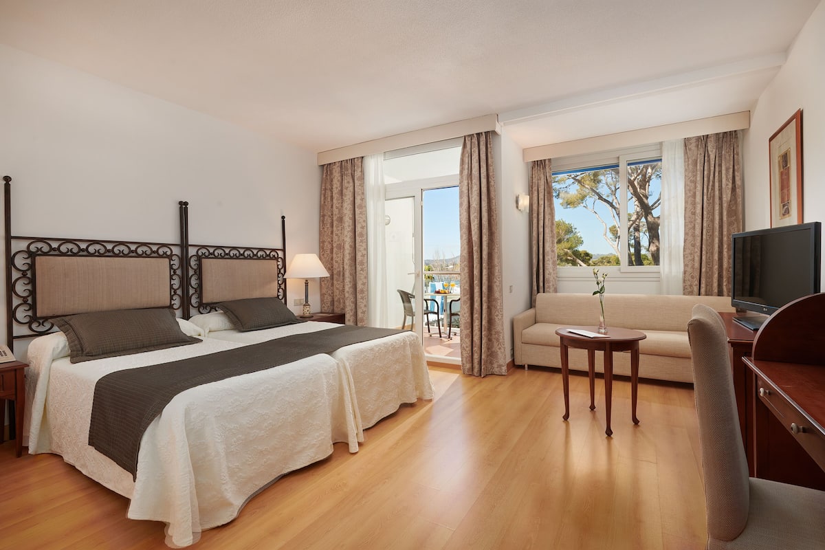 Une chambre d’hôtel avec deux lits, un canapé, une télévision, un bureau et un balcon équipé d’une table et de chaises.