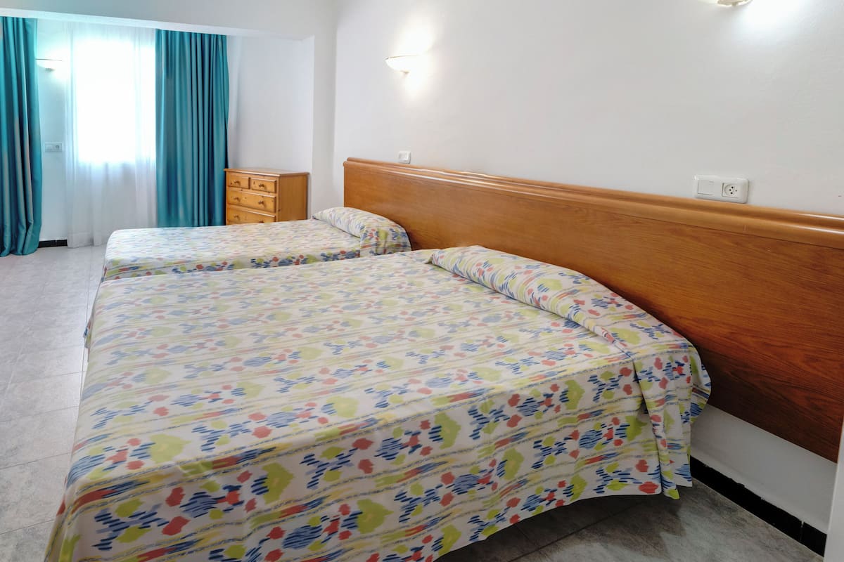 Een hotelkamer met twee bedden, een houten dressoir en een raam met gordijnen.