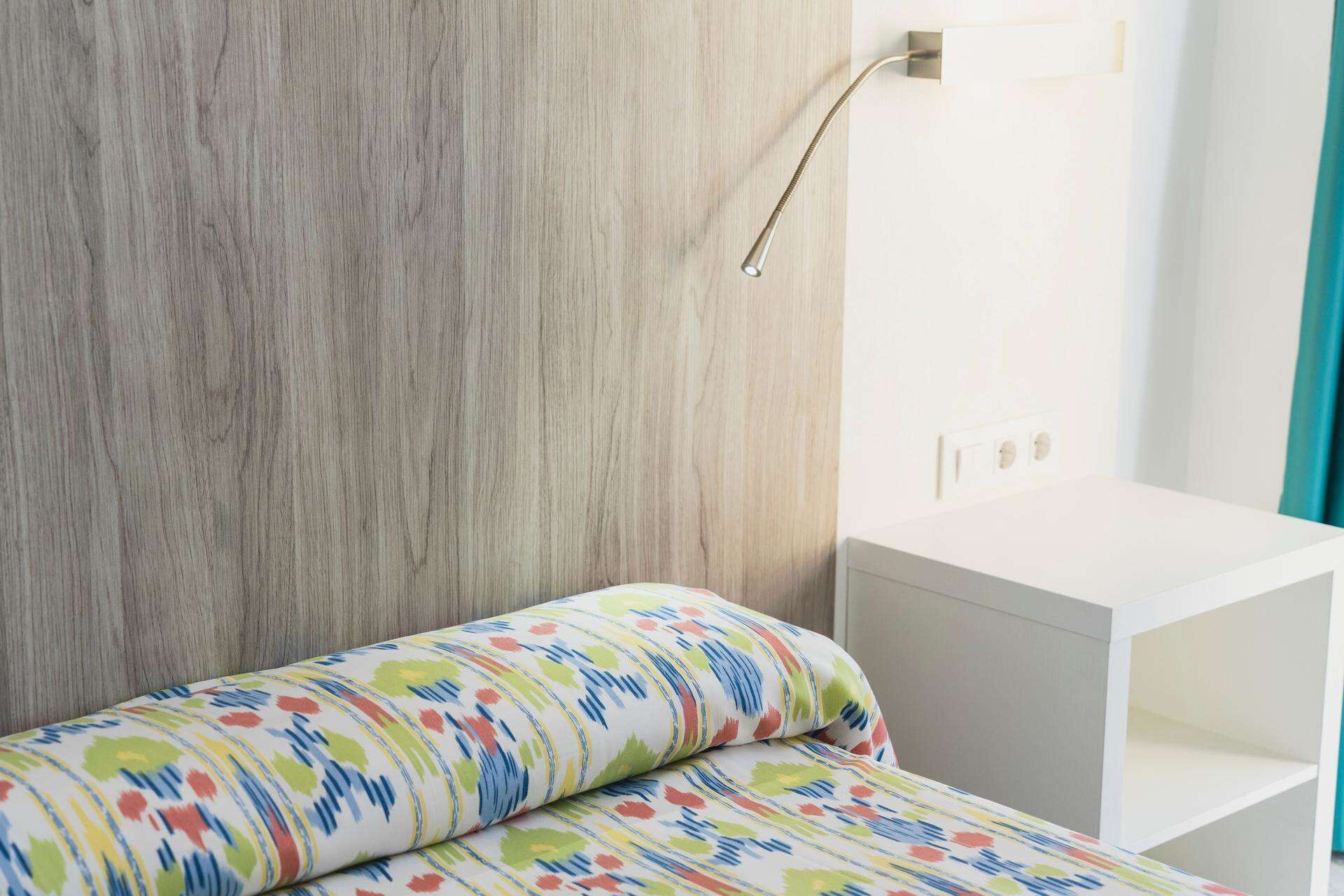 A bedroom with a wooden headboard, a white bedside table, and a colorful bedspread.