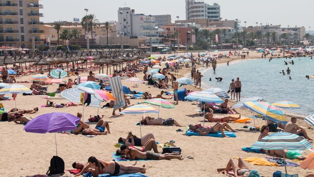 Una playa concurrida, con muchos sombrillas y gente tomando el sol.