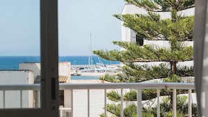 Un balcón con vista al mar y barcos, una silla blanca y un pino.