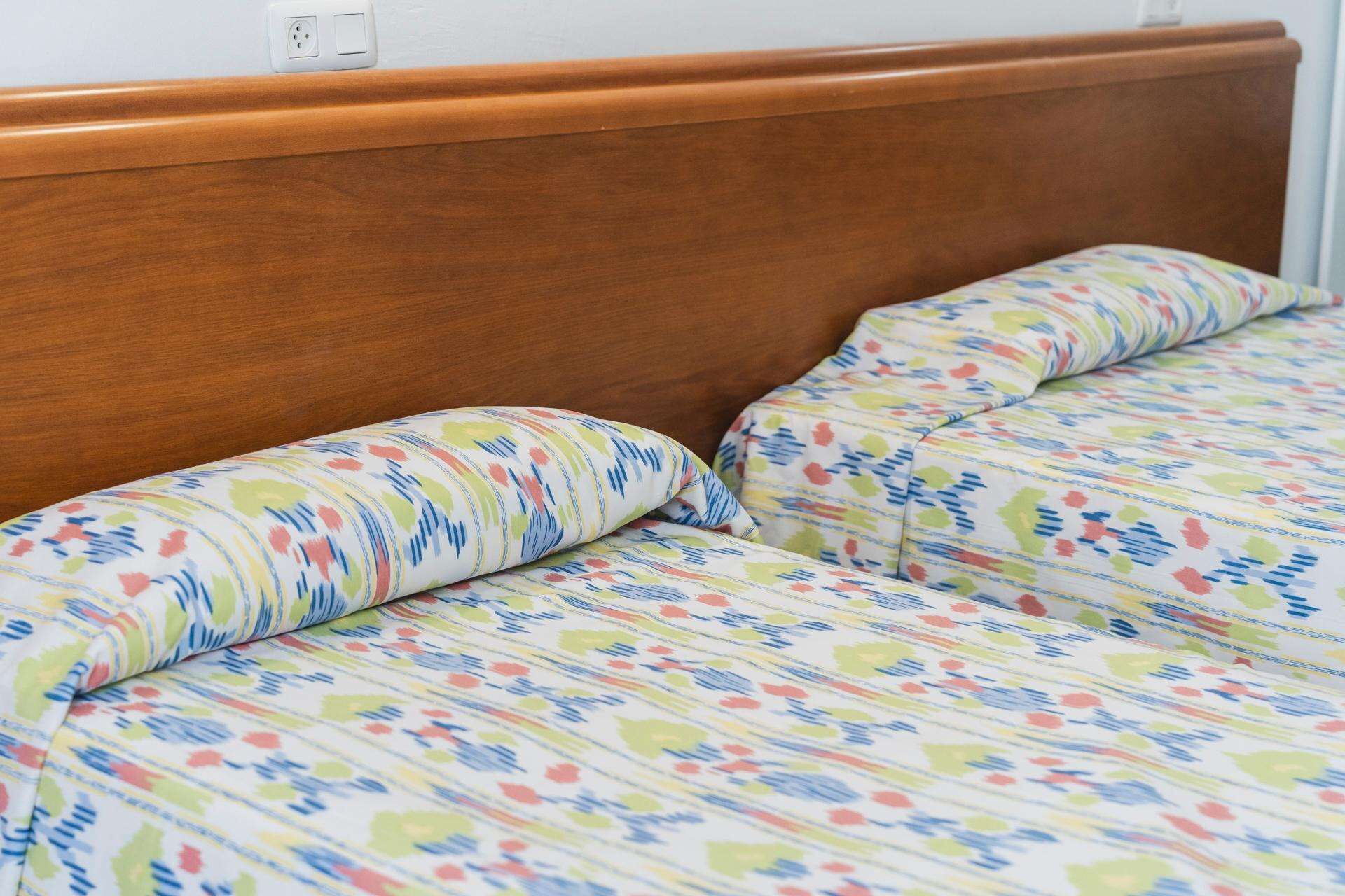 Una cama con cabecera de madera y ropa de cama estampada con motivos florales.