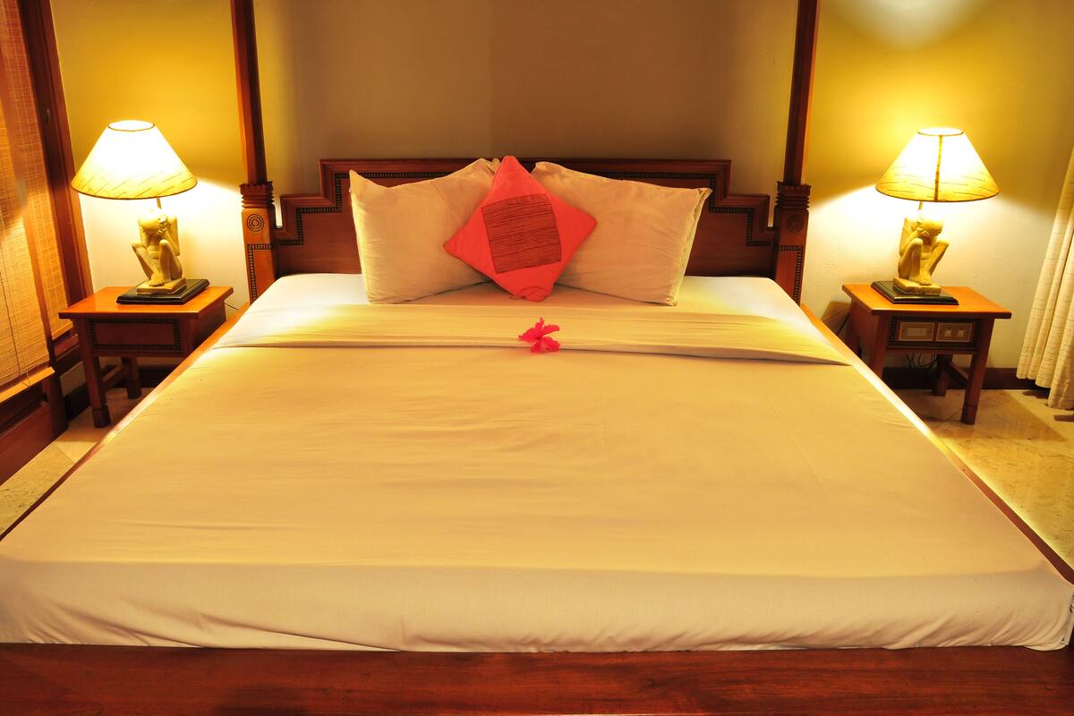 A neatly made bed with white linens, two bedside lamps, and a wooden headboard.