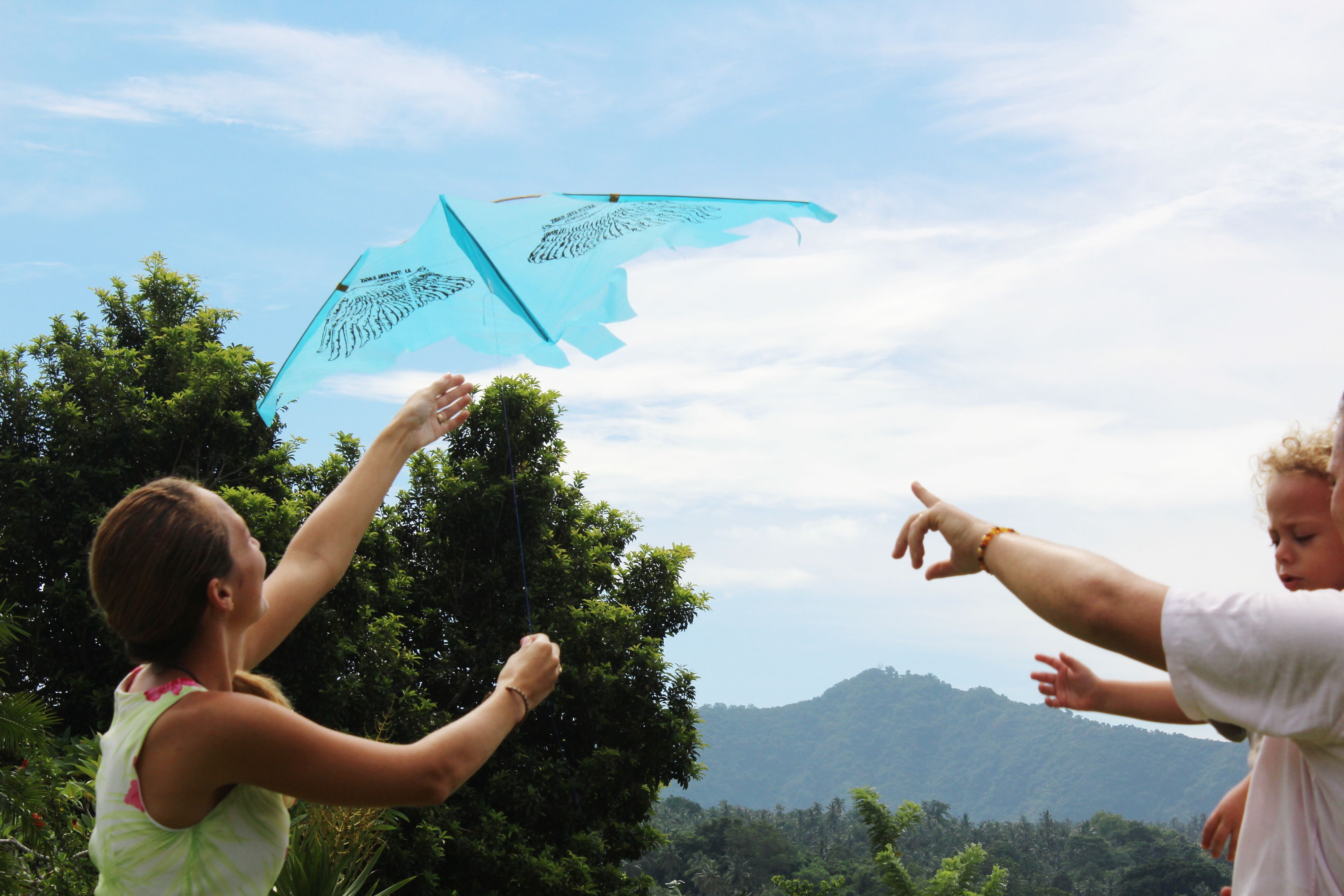 Two people flying a kite in an outdoor setting with trees and a mountain in the background.