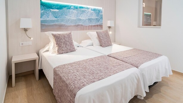 A double bed with two pillows, a bedside table, a wall-mounted lamp, and a large painting of a beach scene. - Hotel Amic Colón (Palma de Mallorca)