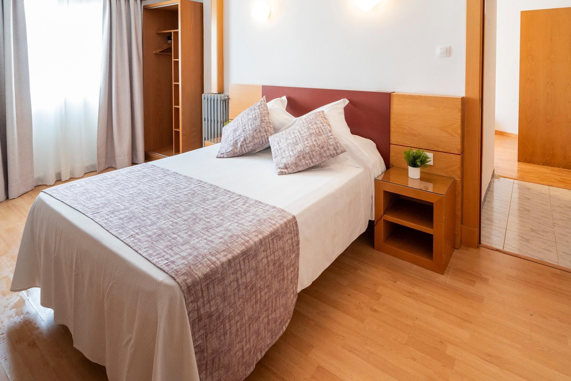 Et pænt indrettet hotelværelse med seng, sengebord og en lille plante.