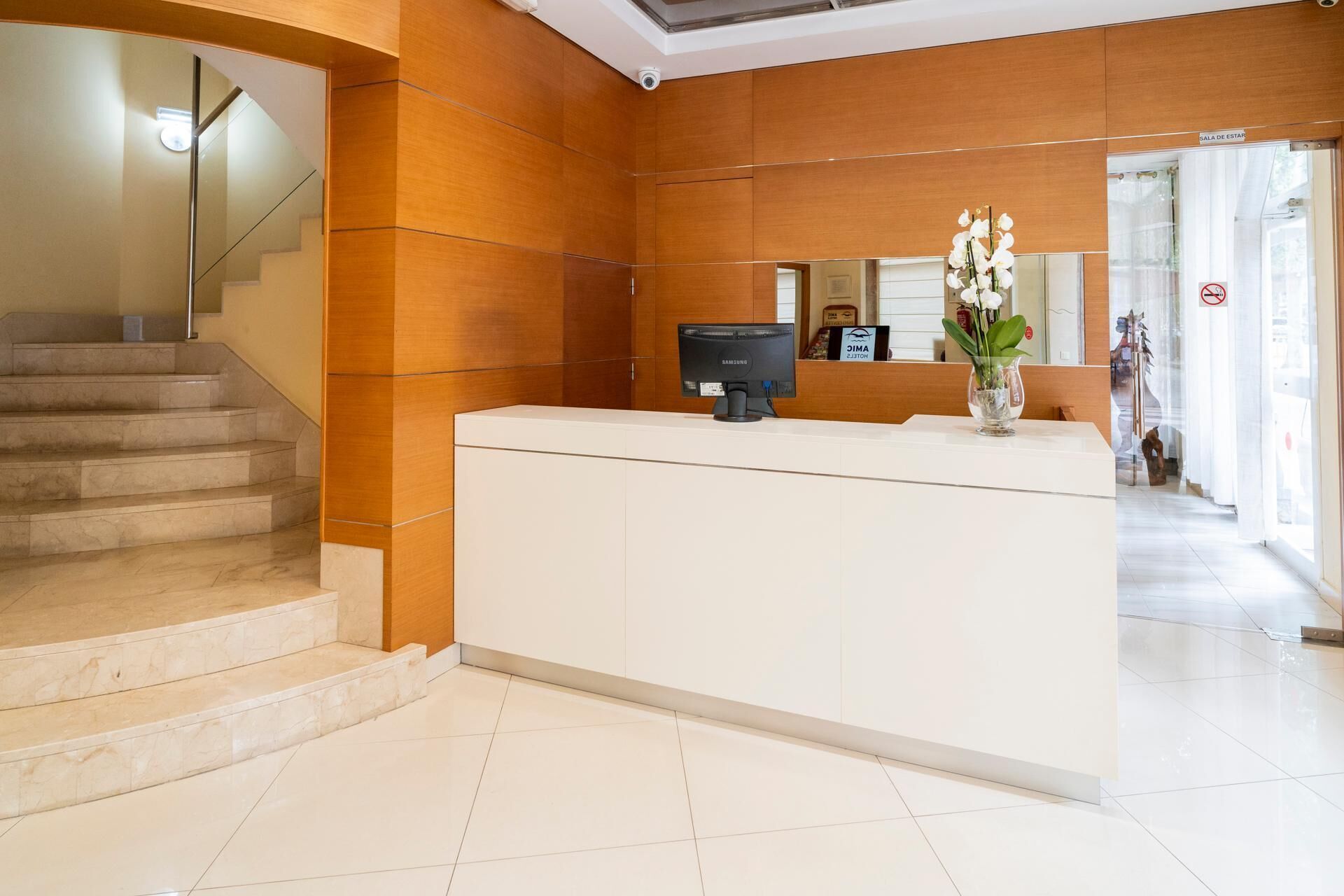 A reception desk with a Samsung monitor, a vase with white flowers, and a staircase.