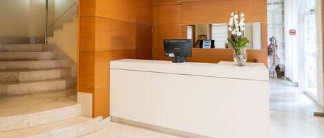 A reception desk with a Samsung monitor, a vase with white flowers, and a staircase.