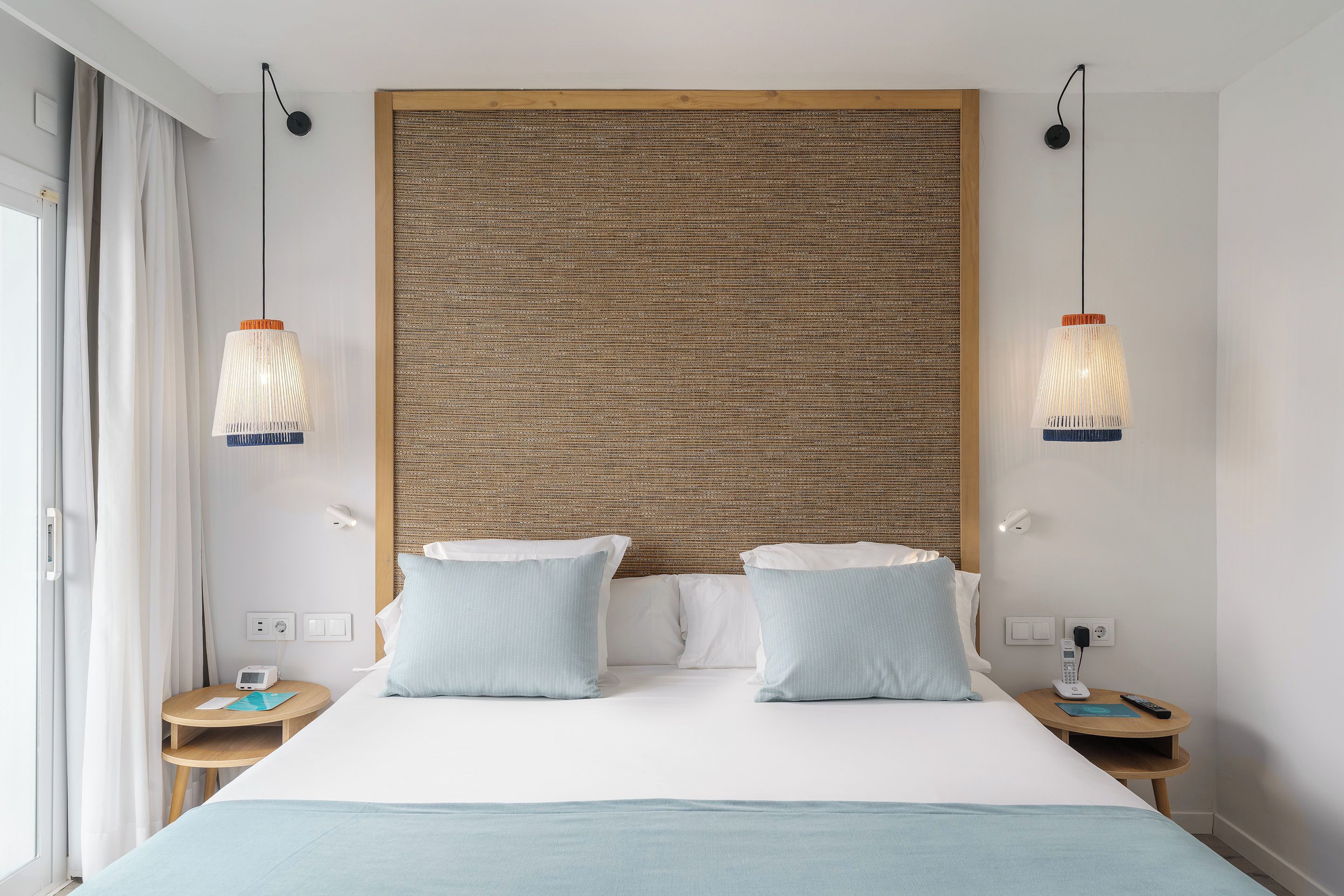 Una habitación de hotel con una cama grande, dos mesitas de noche, una lámpara de pared y una ventana con cortinas.