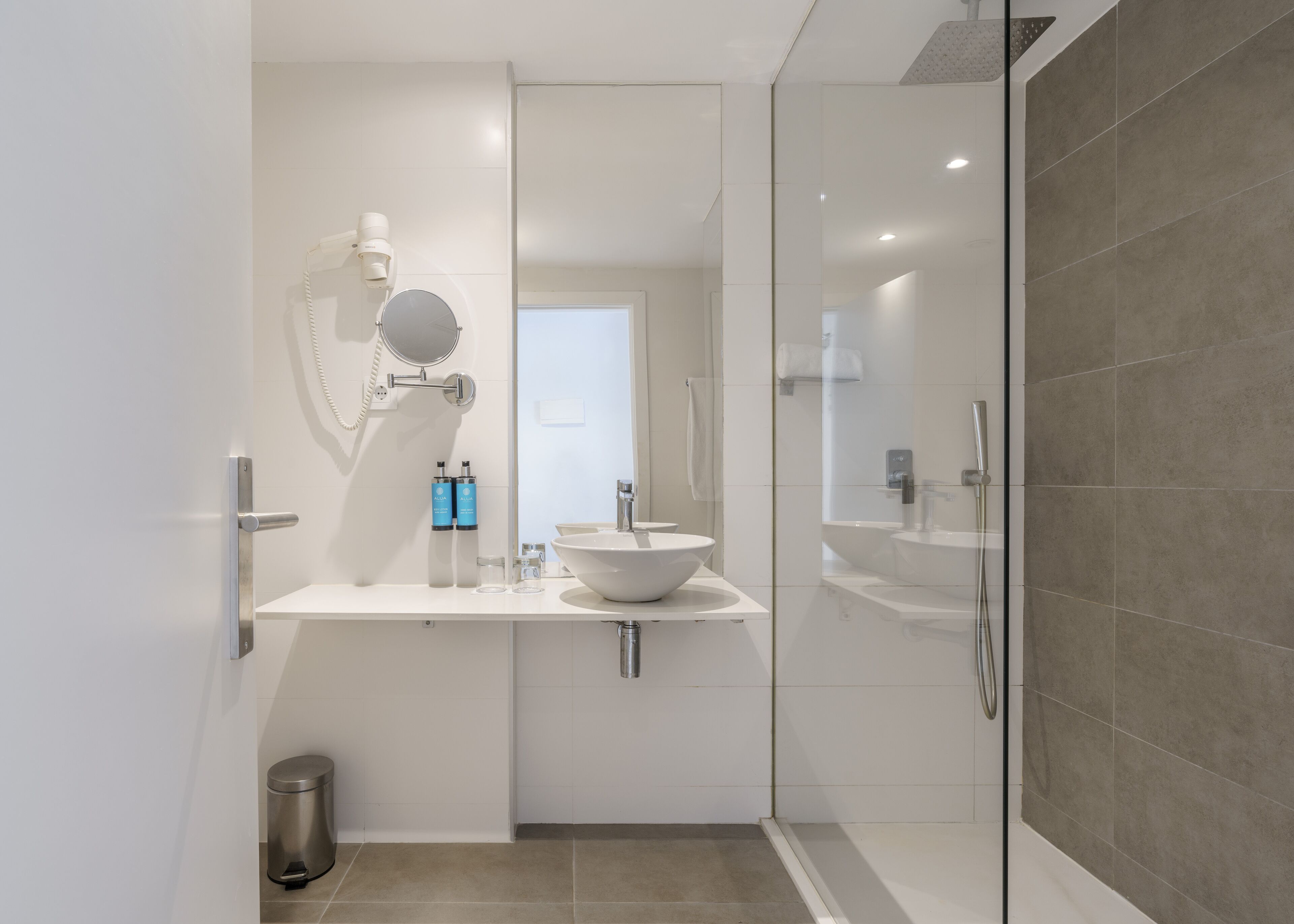 A modern bathroom with a glass-enclosed shower, a large mirror, and a white sink.